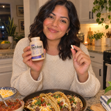 Woman holding Debloat and a capsule before a taco dinner